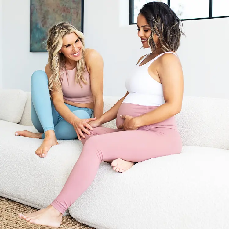 Blond woman sitting on couch with pregnant women wearing yoga clothes talking about hormone harmony